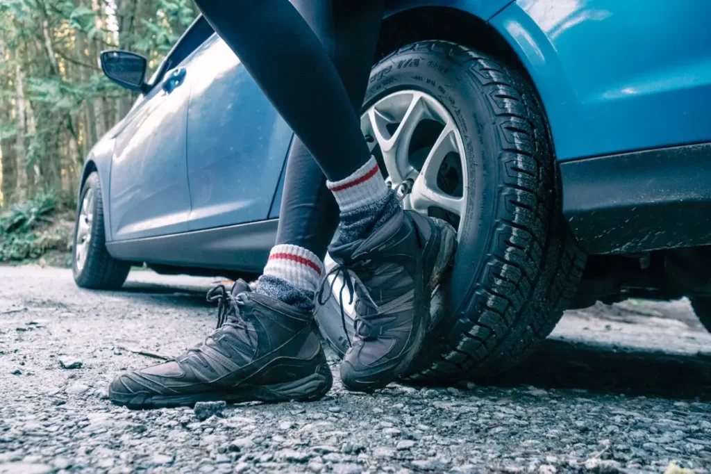 mujer recostada de un coche con sus zapatillass de senderismo en primero plano