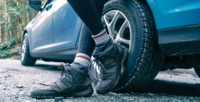 mujer recostada de un coche con sus zapatillass de senderismo en primero plano